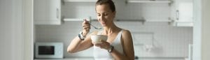 woman in kitchen eating out of a bowl with a spoon