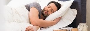 man sleeping in bed with glasses and clock on night stand