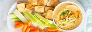 hummus in a bowl next to carrots, celery, and crackers